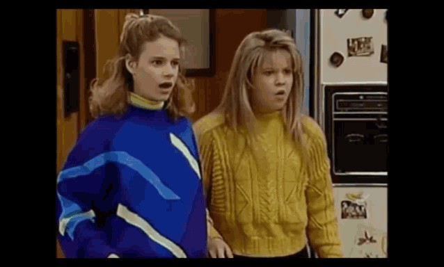 two young women are standing next to each other in front of a refrigerator .