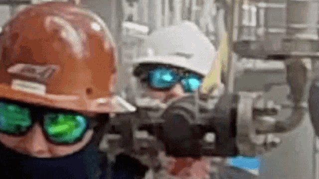a man wearing a hard hat and sunglasses is standing next to another man wearing a hard hat and sunglasses .