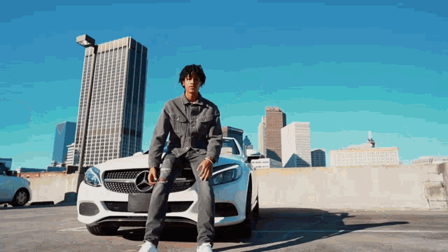 a man is sitting on the front of a white mercedes