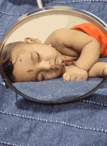 a baby sleeping in front of a mirror with a red spot on his forehead