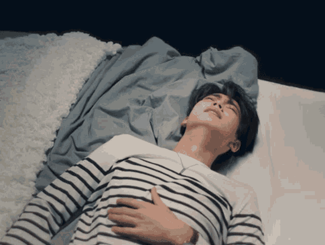 a man in a striped shirt is laying on a bed with his eyes closed