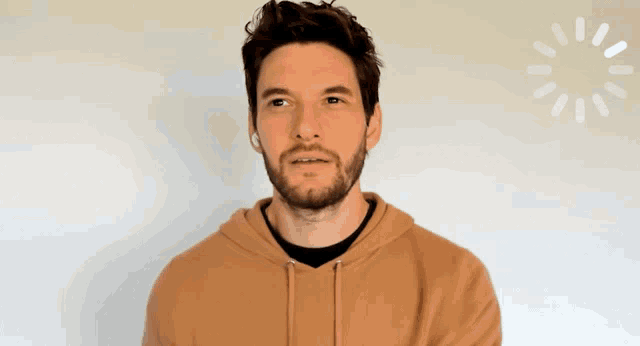 a man with a beard wearing a brown hoodie looks at the camera