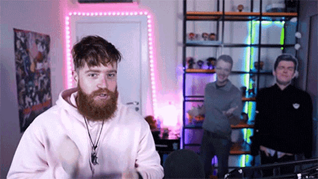 a man with a beard is standing in front of a microphone in a room with two other men .