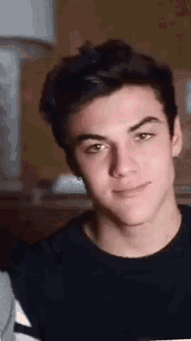 a young man is smiling and looking at the camera while wearing a black t-shirt .