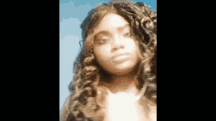 a close up of a woman 's face with curly hair and a blue sky in the background .