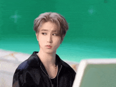a young man in a black jacket is looking at the camera with a green background .