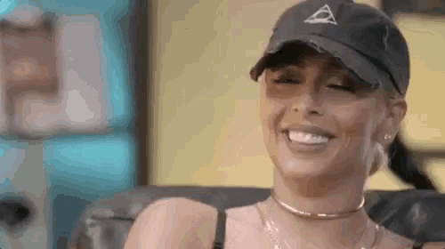 a woman wearing a hat and choker is sitting on a couch and smiling .