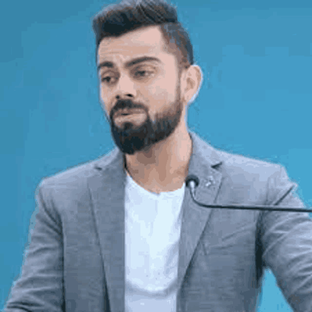 a man with a beard is standing in front of a microphone in a suit .