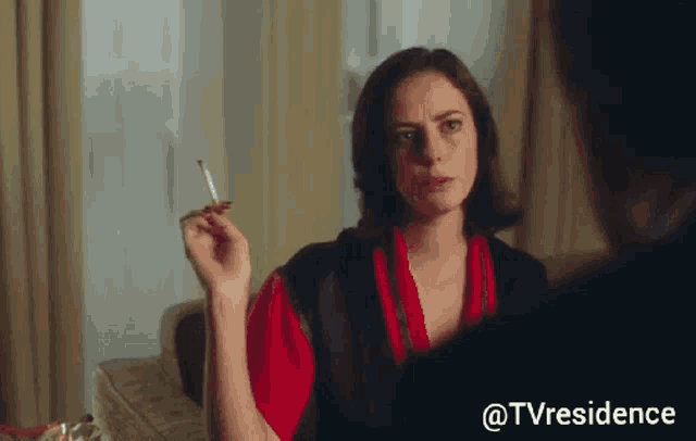 a woman in a red robe is smoking a cigarette in a room