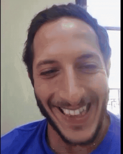 a man with a beard wearing a blue shirt is smiling for the camera