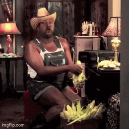 a man wearing overalls and a cowboy hat is sitting in a living room holding corn