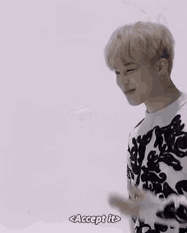 a young man in a black and white sweater is standing in front of a white wall and waving his hands .