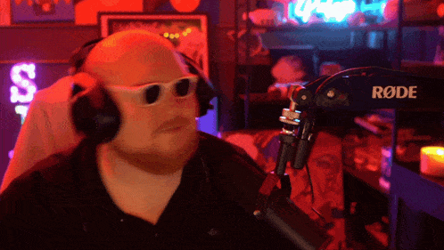 a man wearing headphones and sunglasses is standing in front of a rode microphone