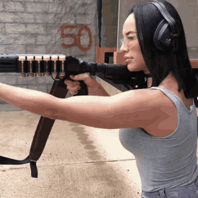 a woman wearing headphones is holding a gun in front of a brick wall with the number 50 written on it