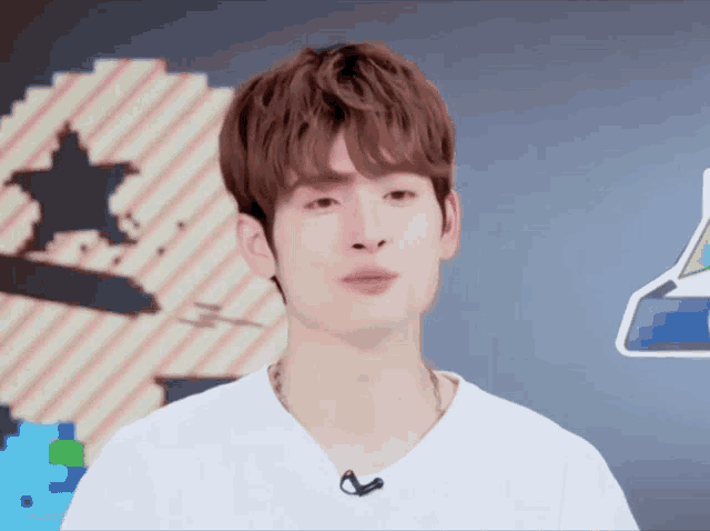 a young man wearing a white shirt with a microphone on his neck looks at the camera