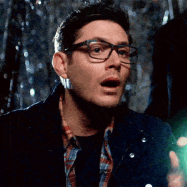 a man wearing glasses and a plaid shirt is holding a green light in his hand .