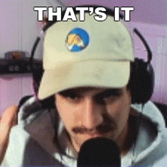 a man wearing a hat and headphones is standing in front of a microphone .