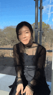 a woman sitting on a balcony wearing a black dress and sheer top