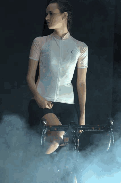 a woman is sitting on a bike in a dark room with smoke behind her