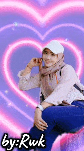 a girl wearing a hijab and a white hat is sitting on a stump with a pink heart in the background