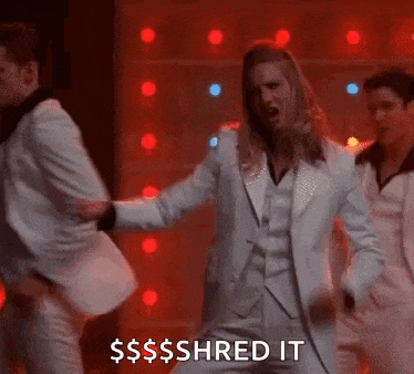 a man in a white suit is dancing on a stage while another man looks on .