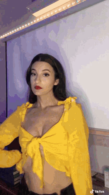 a woman wearing a yellow crop top has a tiktok sticker on her shoulder
