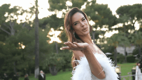 a woman in a white feathered dress holds her hand out