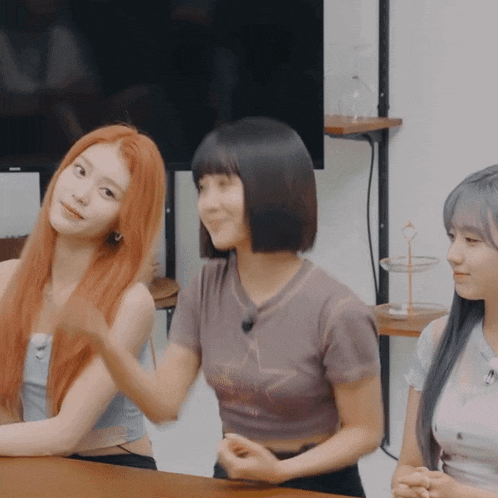 three women are sitting at a table and one of them is wearing a shirt that says ' i love you '