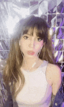 a young woman wearing headphones and a white tank top is standing in front of a mirror .