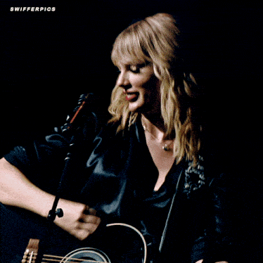 a woman singing into a microphone while holding a guitar with swifterpics written on the bottom right