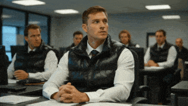 a man in a black vest sits in a classroom