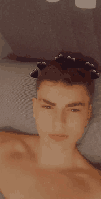 a shirtless young man is laying on a bed with hearts on his head