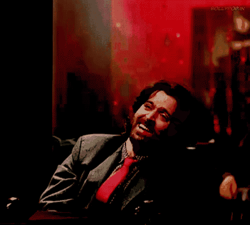 a man in a suit and tie is smiling in front of a red background that says bollypop.in on it