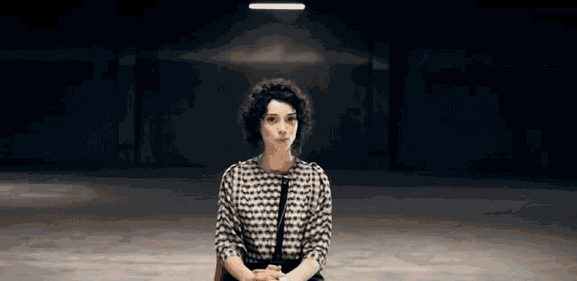 a woman in a black and white dress is sitting in a dark room