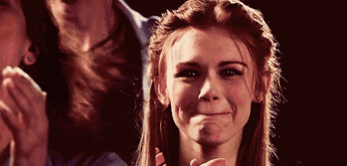 a woman with red hair is smiling and making a funny face while a man applauds behind her .