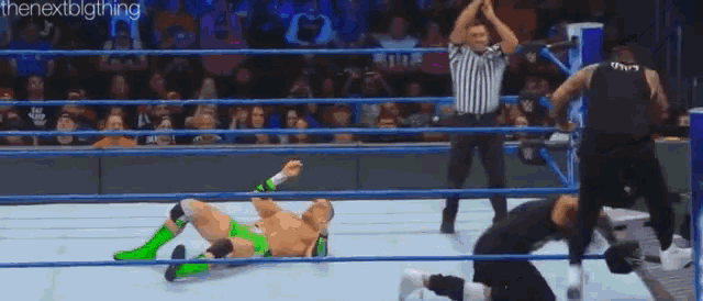 a wrestler is laying on the ground in a wrestling ring while a referee stands behind him .