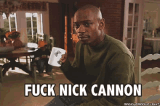 a man sitting at a table with a cup of coffee and the words fuck nick cannon on the screen