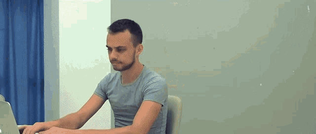 a man is sitting at a desk typing on a laptop .