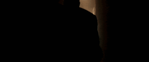 a man is walking down a dark alleyway with a light at the end of it .