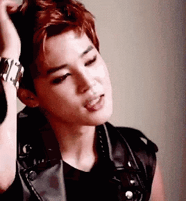 a young man wearing a leather vest and a watch is looking down .