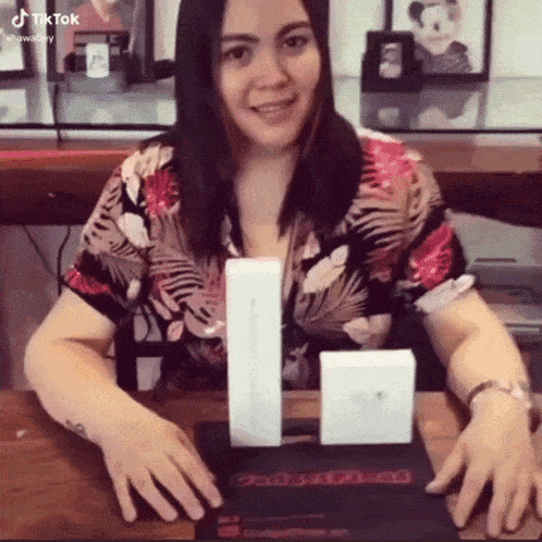 a woman in a floral shirt is sitting at a table with two boxes .