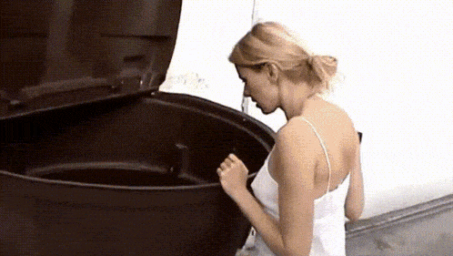 a woman in a white tank top is standing next to a black trash can .