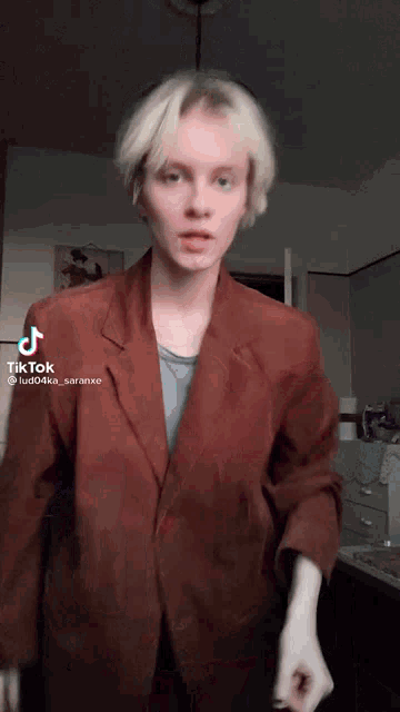 a woman with blonde hair is wearing a brown jacket