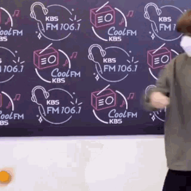a man wearing a mask is standing in front of a blackboard with logos for kbs fm 106.1