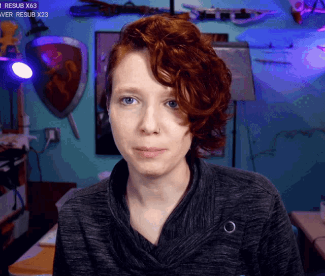 a woman with red hair stands in front of a wall with shields and a sign that says resub x23