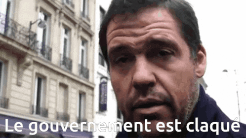 a man is standing in front of a building with the words le gouvernement est claque written below him