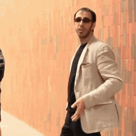 a man in a suit and sunglasses is standing in front of a brick wall .