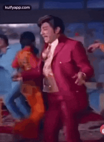 a man in a red suit is dancing in a room while another man stands behind him .