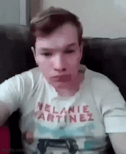 a young man is sitting on a couch wearing a white t-shirt with the name melanie martinez on it .