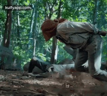 a man is kneeling in the dirt in the woods .